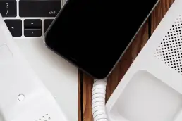 Close up of a work desk with a keyboard, pen, mobile phone and phone system.